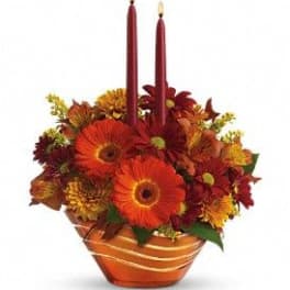 Orange and red floral centerpiece with two burgundy candles in a striped bowl