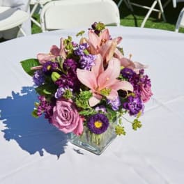 Pink and purple floral centerpiece in a square glass vase