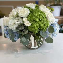 White roses and green hydrangeas in a glass vase with blue hydrangea accents