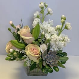 Pastel roses and white blooms arranged in a square glass vase