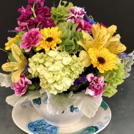 Colorful mixed flower arrangement in a white teacup on a patterned saucer