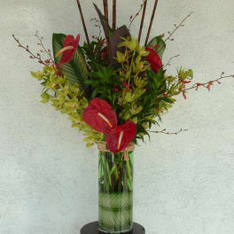 Tropical flower arrangement in a tall glass vase with red anthuriums