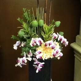 Tall floral arrangement with orchids and a yellow bloom in a black vase