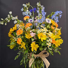 Mixed bouquet of yellow, blue, and orange flowers in a glass vase with a ribbon