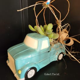 Succulent arrangement in a turquoise ceramic truck planter with a small bird topper