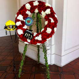 Red and white floral wreath on an easel with a firefighter helmet and gloves