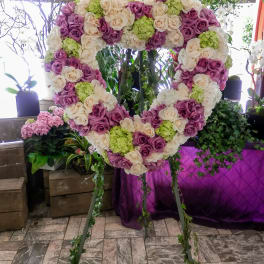 Heart-shaped floral display of pink, cream, and green roses on a stand