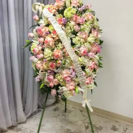 Standing funeral wreath of pink and white flowers with a condolence ribbon