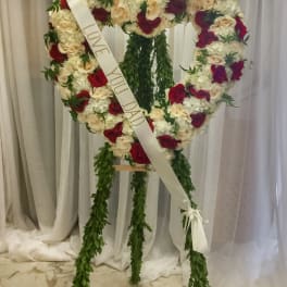 Heart-shaped rose wreath with a memorial ribbon on a stand
