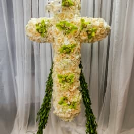 Cross-shaped floral arrangement of cream roses and green orchids with trailing greenery