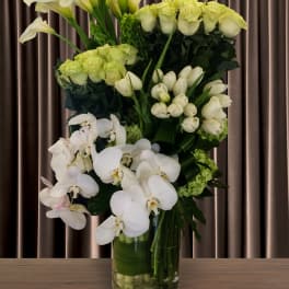 Tall white floral arrangement with calla lilies, roses, and orchids in a glass vase