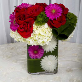 Red roses and pink daisies in a green vase with white hydrangeas
