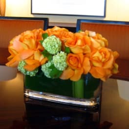 Orange roses arranged in a square glass vase with green blooms