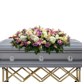 Floral casket spray with pink, purple, and white flowers on a gray casket