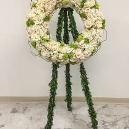 Circular floral wreath on a stand with cream roses and green accents