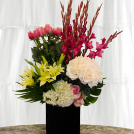 Tall floral arrangement with pink, yellow, white, and red blooms in a black vase