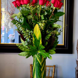 Tall vase arrangement of red roses with mixed greenery