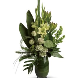 Tall green floral arrangement in a glass vase with lotus pods and lilies