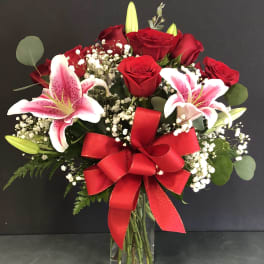 Arrangement of red roses and pink lilies with baby's breath in a clear vase with a large red bow