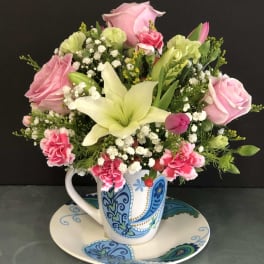 Pink roses and lilies arranged in a patterned mug on a matching saucer