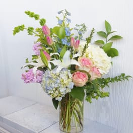 Mixed bouquet of pink roses, white lilies, and hydrangeas in a glass vase