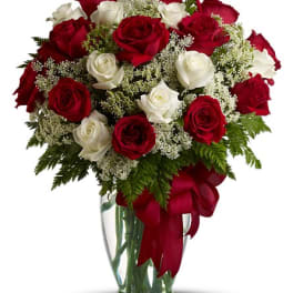 Red and white roses arranged in a clear glass vase with a red ribbon