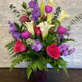 Bouquet of pink roses, white lilies, and purple flowers in a purple vase