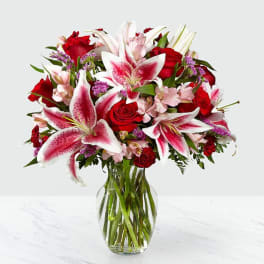 Bouquet of pink lilies and red roses in a clear glass vase