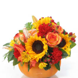 Autumn bouquet of sunflowers, roses, and carnations in an orange bowl vase