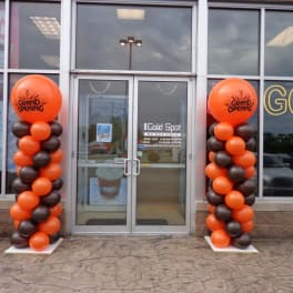 Orange and black balloon columns flank a storefront entrance