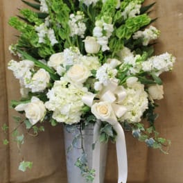 White roses and hydrangeas in a tall silver vase with a ribbon