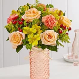 Peach roses and yellow flowers arranged in a pink glass vase