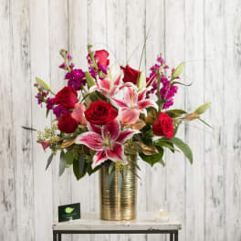 Red roses and pink lilies in a gold vase with a small candle