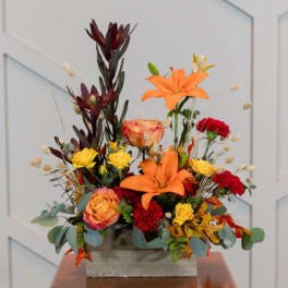 Mixed floral arrangement with orange lilies and roses in a wooden box