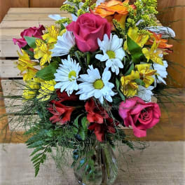 Mixed bouquet of roses, daisies, and yellow alstroemeria in a glass vase
