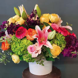 Colorful arrangement of lilies, roses, hydrangeas, and other blooms in a white ceramic vase