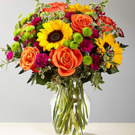 Bouquet of orange roses, sunflowers, and magenta mums in a glass vase