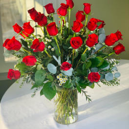 Red roses arranged in a clear glass vase with small white filler flowers