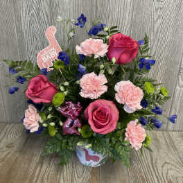 Pink roses and carnations with blue flowers in a baby-themed container