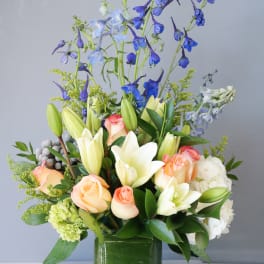 Mixed bouquet of lilies, roses, and blue delphinium in a glass vase