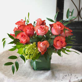 Coral roses arranged in a square vase with green foliage