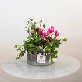 Oval metal planter with pink flowers, white blooms, and a small bird figurine.