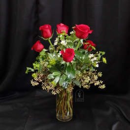 Red roses arranged in a clear glass vase with greenery and small white filler flowers