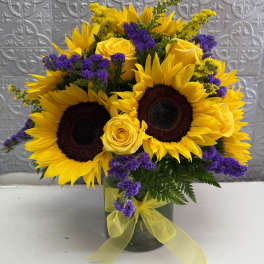 Sunflower and yellow rose bouquet in a glass vase with purple accents
