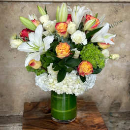 Bouquet of white lilies, roses, and hydrangeas in a green glass vase
