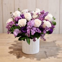 White roses and purple lilacs in a white ribbed vase
