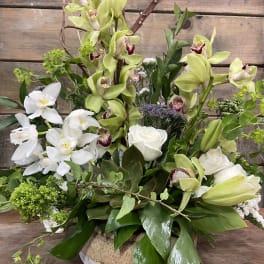 Mixed floral arrangement with white and green orchids and roses in a low container