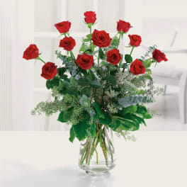 Tall arrangement of long-stem red roses with lush filler in a clear glass vase