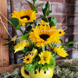 Yellow sunflower arrangement in a smiley-face mug with a small bird figurine
