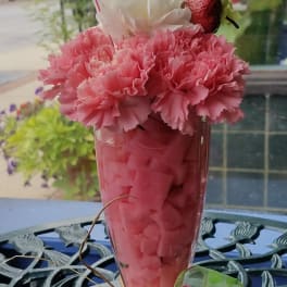 Milkshake-style floral arrangement with pink and white carnations, straws, and a polka dot ribbon butterfly.